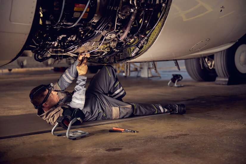 Fluggerätemechaniker am Boden liegend beim Warten eines Triebwerks | © Envato Elements Fluggerätemechaniker am Boden liegend beim Warten eines Triebwerks | © Envato Elements